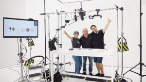 This type of B2B project illustrates "what is commercial photography?". Inside Sum Effect Studio, standing amid the photography and filming equipment at the end of a studio filming session we see the jubilant team and a business owner at the end of a multi-day project Standing and facing the camera with thumbs up, from the left is a female, and then two males. The male in the middle is the business owner, who commissioned our team to make product videos.